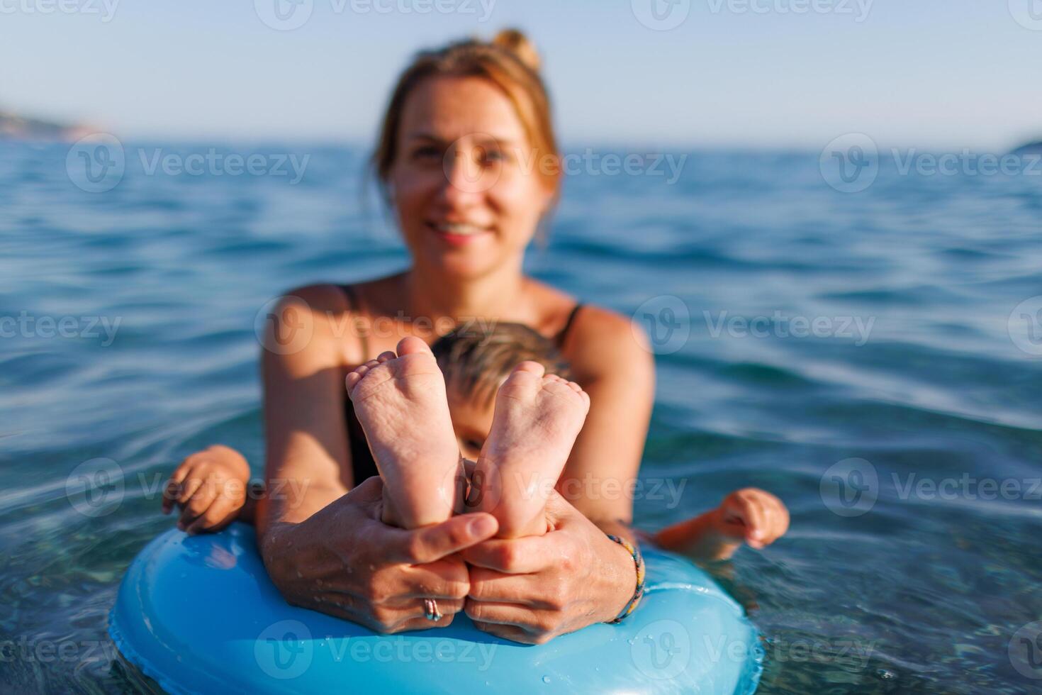 A young mother shows the legs and arms of her baby, who is sitting in an inflatable ring in the seaYoung mother baby legs arms inflatable ring sea photo