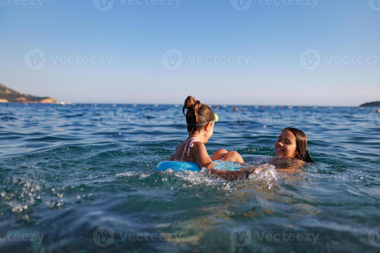 Two sisters in bathing suits play with an inflatable ring in the seaTwo sisters play with inflatable ring seaTwo sisters play with inflatable ring seaTwo sisters play with inflatable ring sea photo