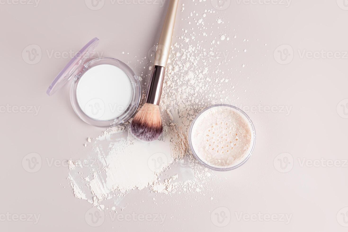 Two open packs of compact and loose powder in a light, white matte tone with a makeup brush and a powder sample on a light background. top view. photo