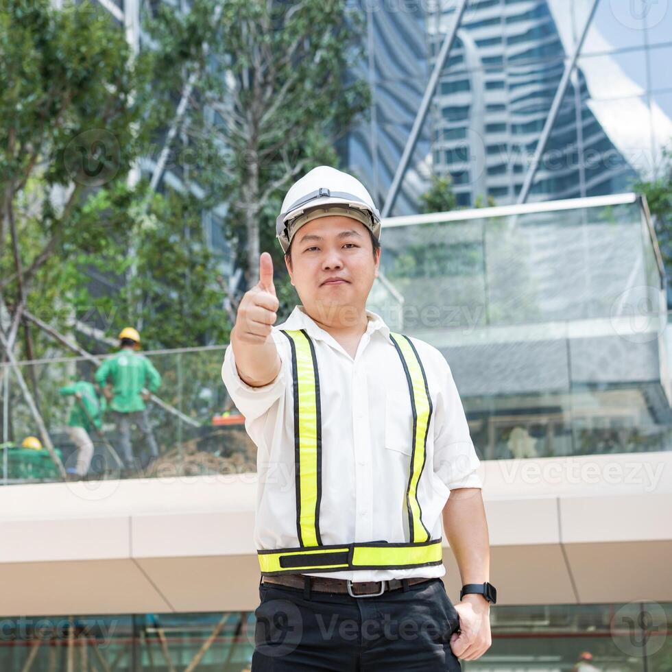 With a bright smile and a thumbs up a smiling Asian construction professional acknowledges success at a contemporary building site. b photo