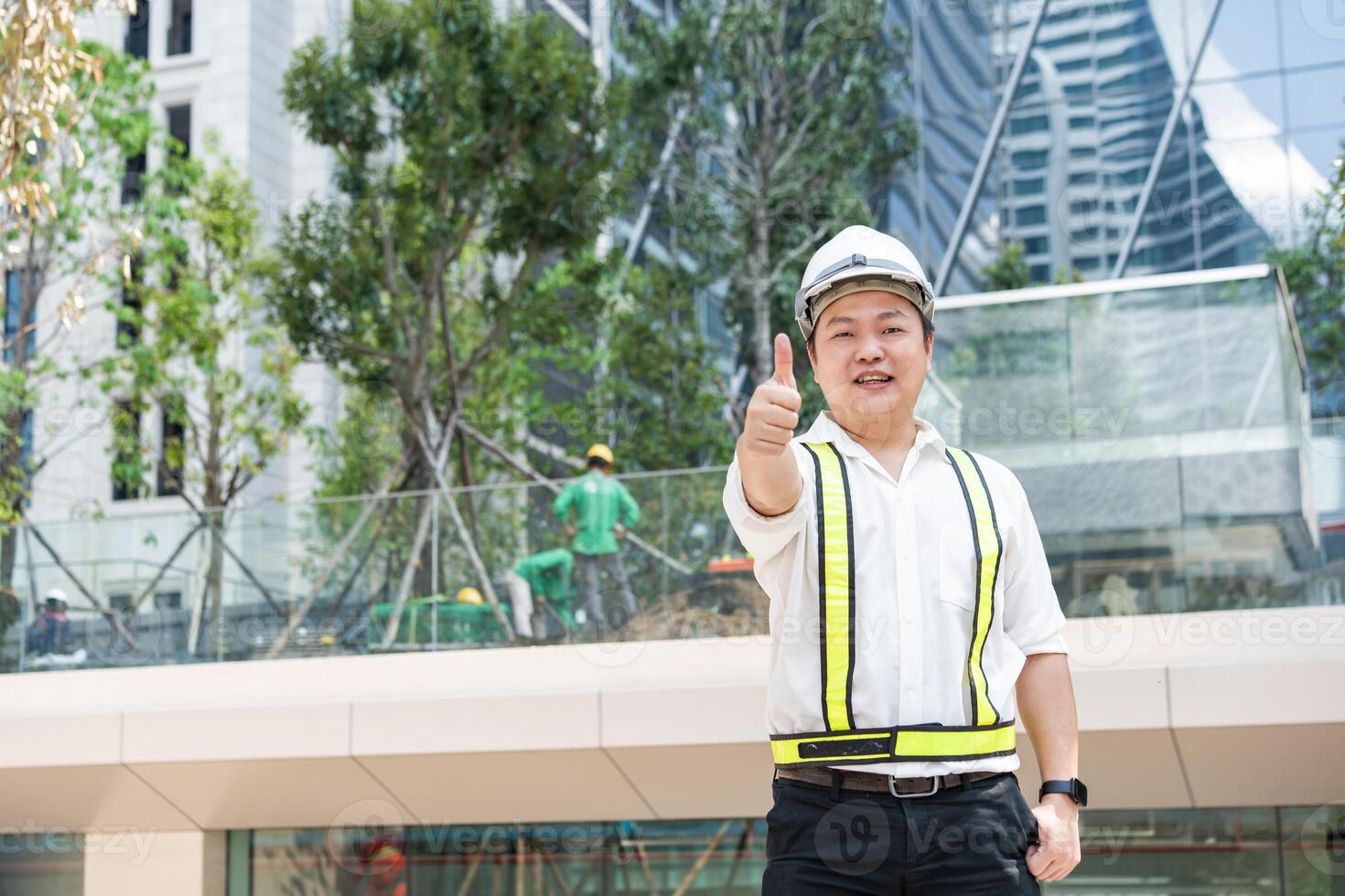 With a bright smile and a thumbs up a smiling Asian construction professional acknowledges success at a contemporary building site. a photo