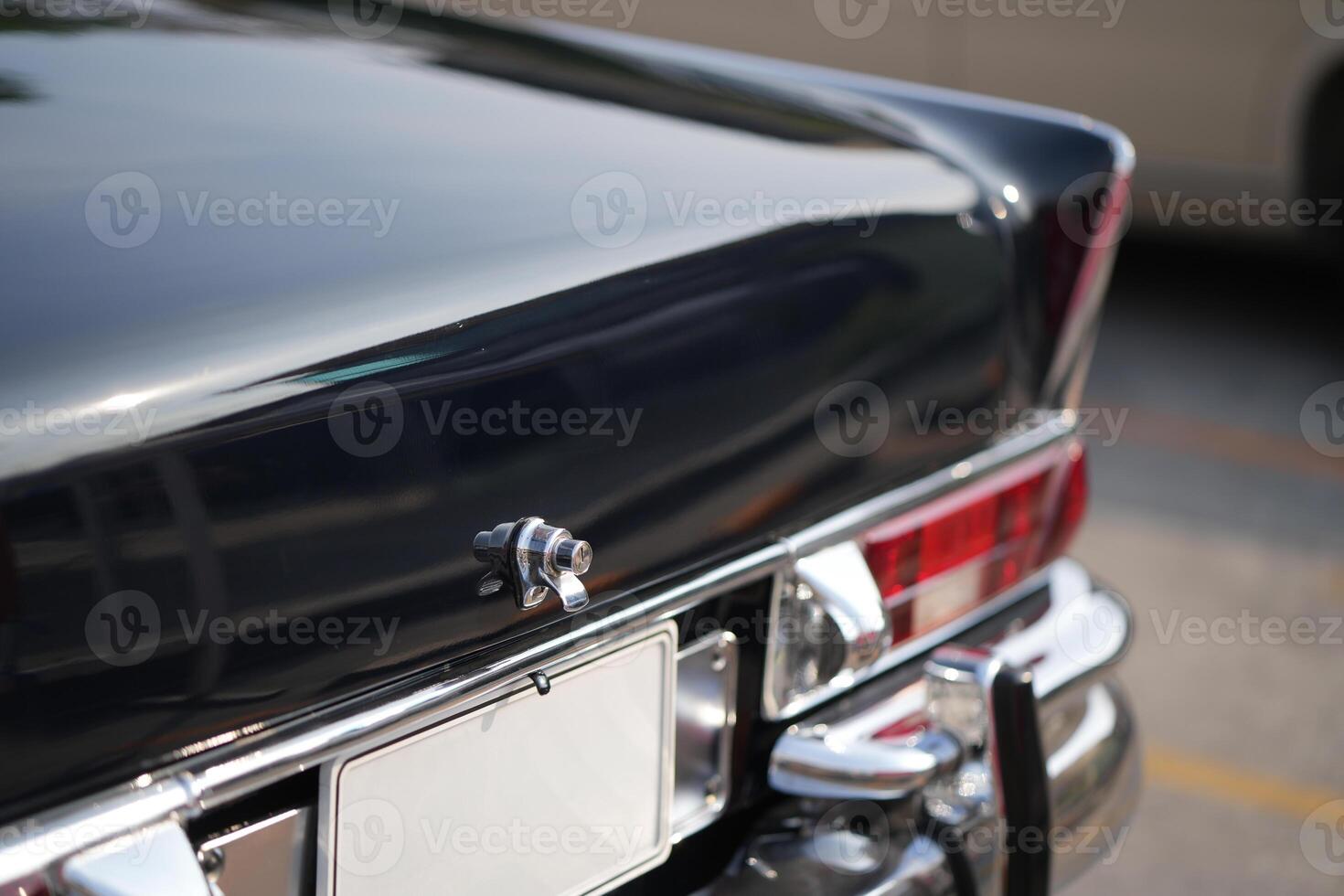 A chrome keyhole above the license plate and a polished rear trunk lock system on a vintage car highlight its sturdy and secure mechanical design.g photo