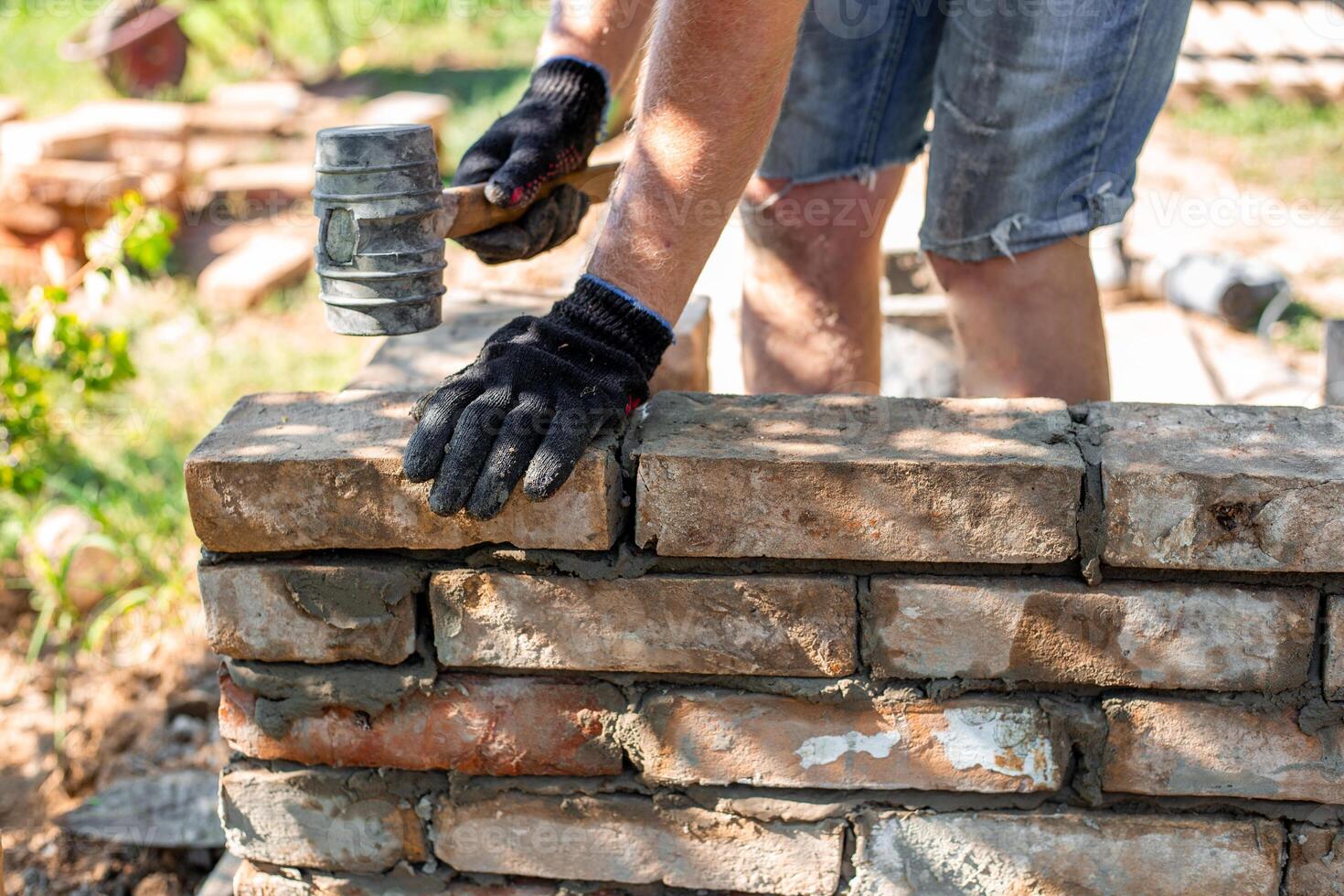 A worker wearing a glove hits a brick with a rubber mallet, ensuring that it is firmly fixed to a new brick wall photo