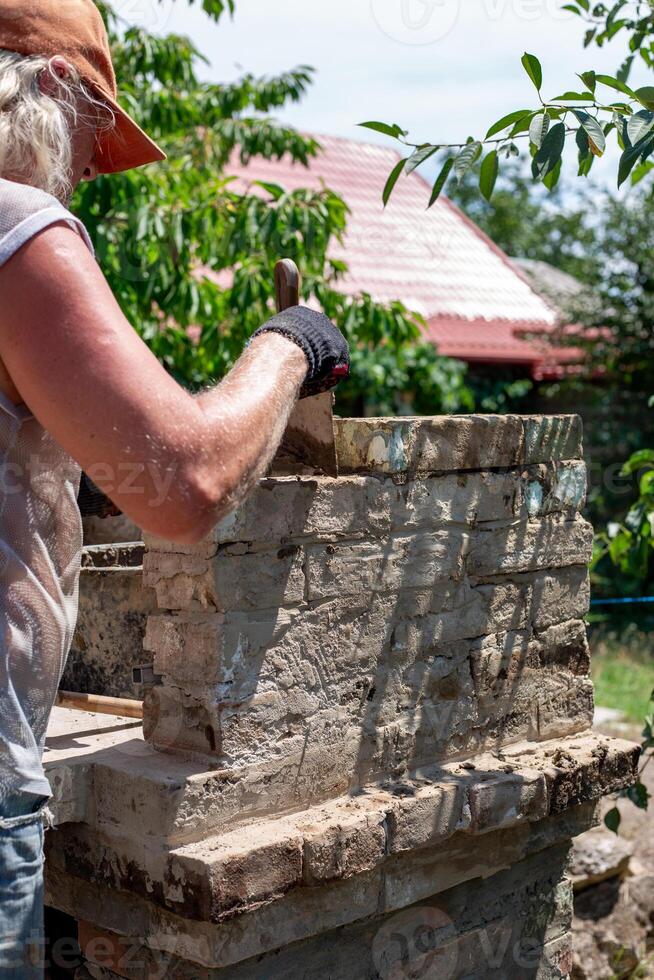 Man applying cement mortar to bricks to build a brick oven barbecue in the backyard, home improvement photo
