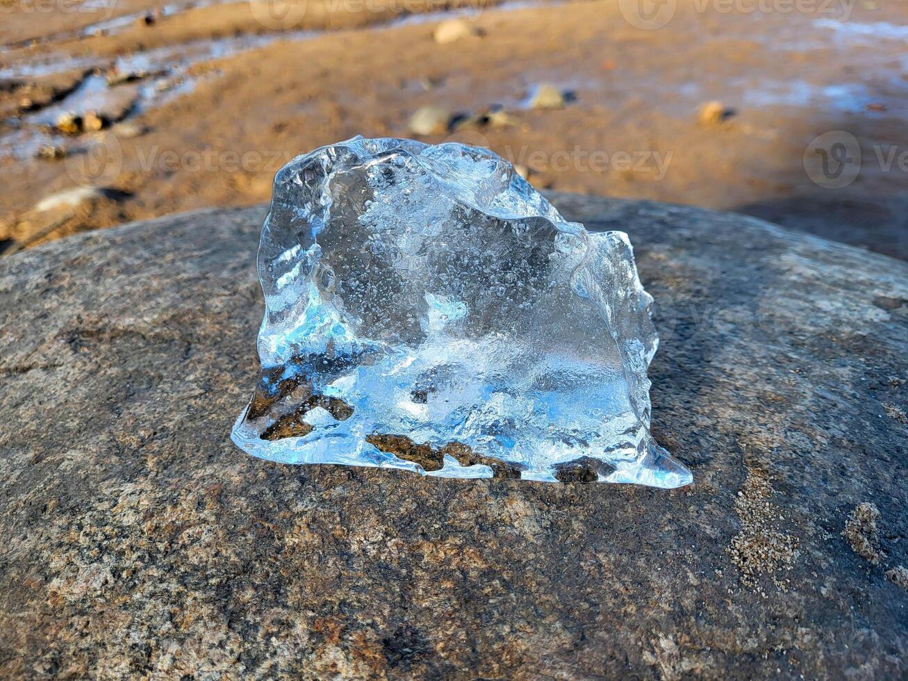 A piece of blue transparent ice lies on a rock on the shore. photo
