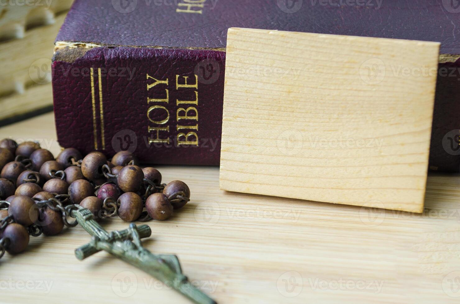 The Holy Bible and Holy Rosary placed beside wooden block with customizable space for text or message sharing. Religion and Christianity concept photo