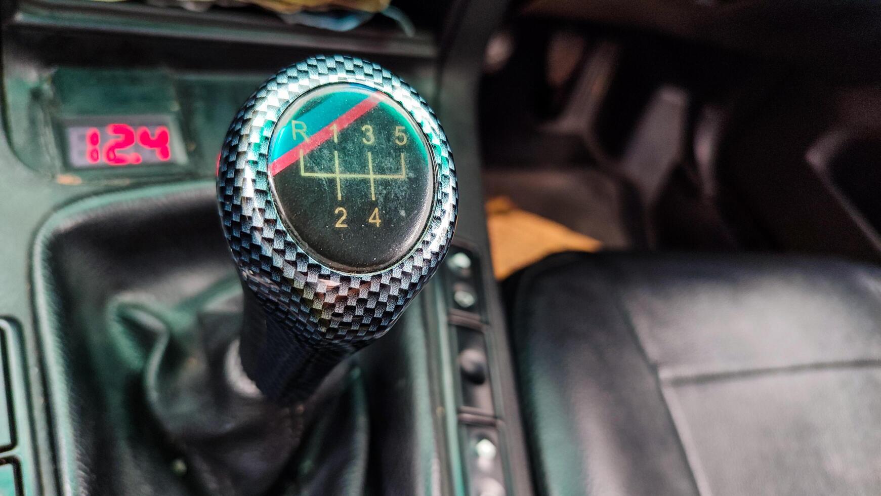 Closeup shows the car's manual gear shift knob, with a checkered pattern and a clear diagram of the 5-speed gear shift pattern with reverse gear. photo
