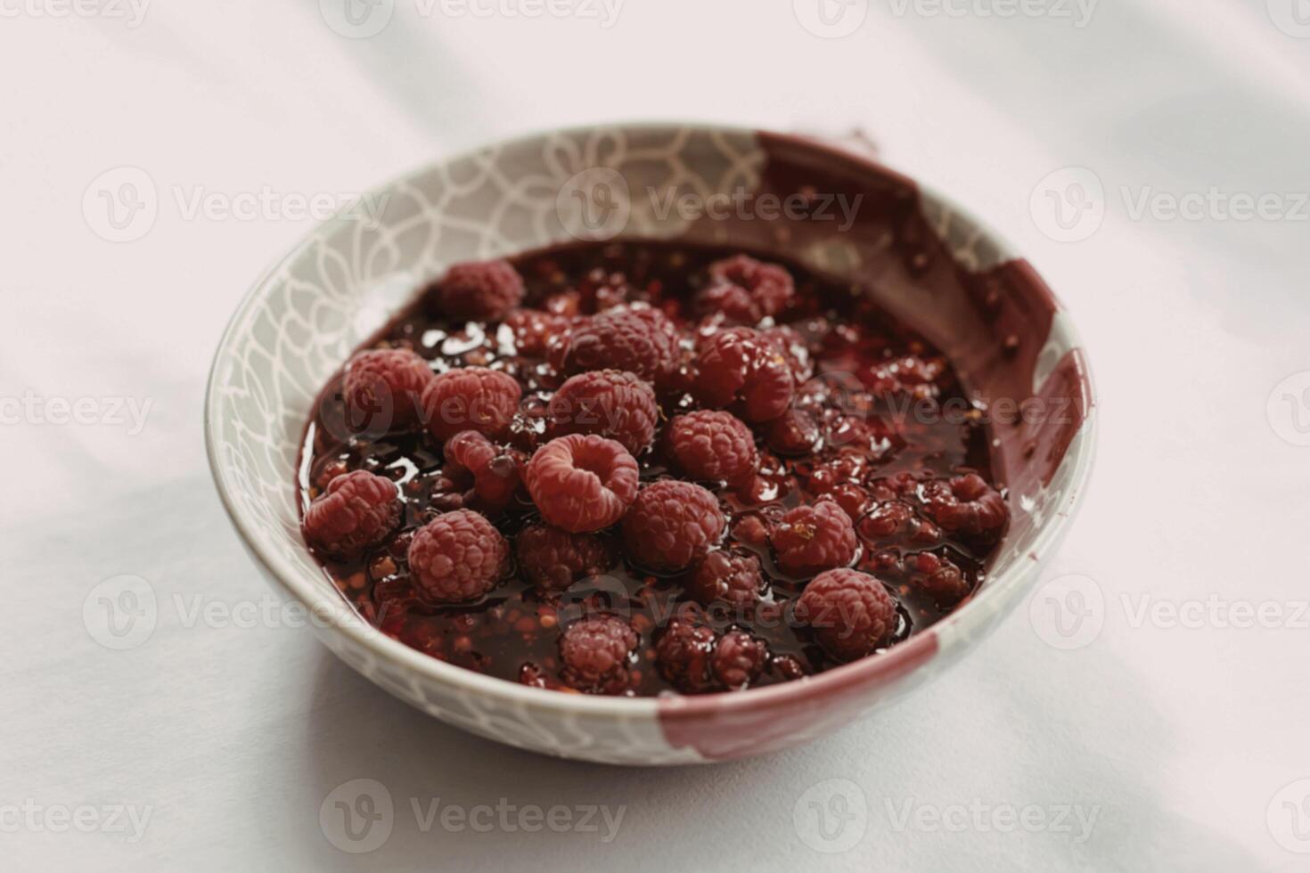 A photograph of a ceramic bowl filled with glistening raspberry jam photo