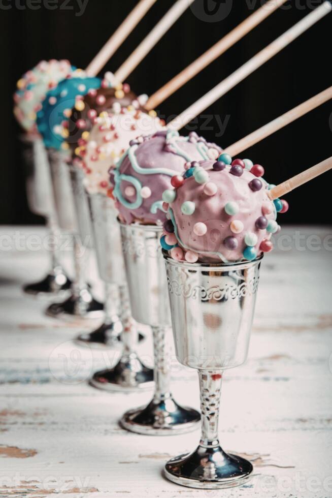 Colorful cake pops in the metal wineglasses on a wooden table photo