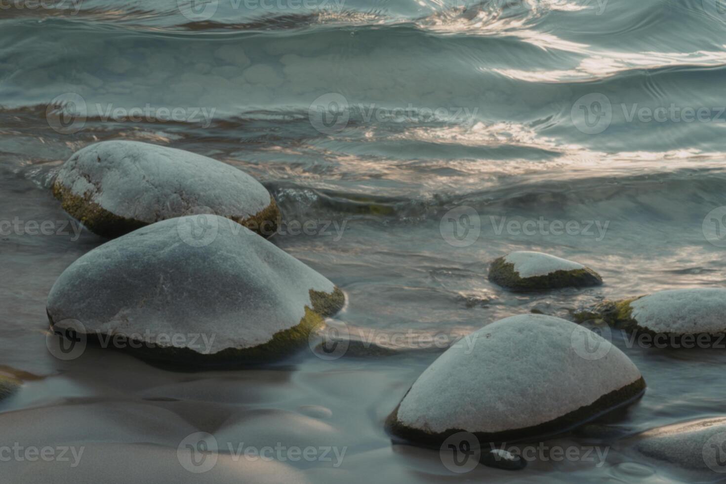A photograph of weathered gray rocks jutting out from turbulent turquoise water. photo