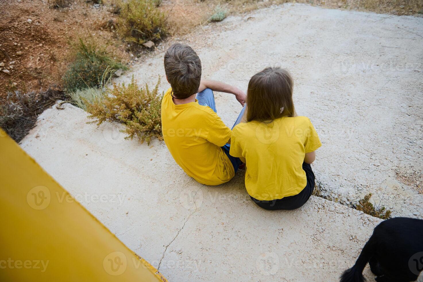 Two Individuals Sitting Outdoors in Yellow Shirts Amid a Natural Landscape photo