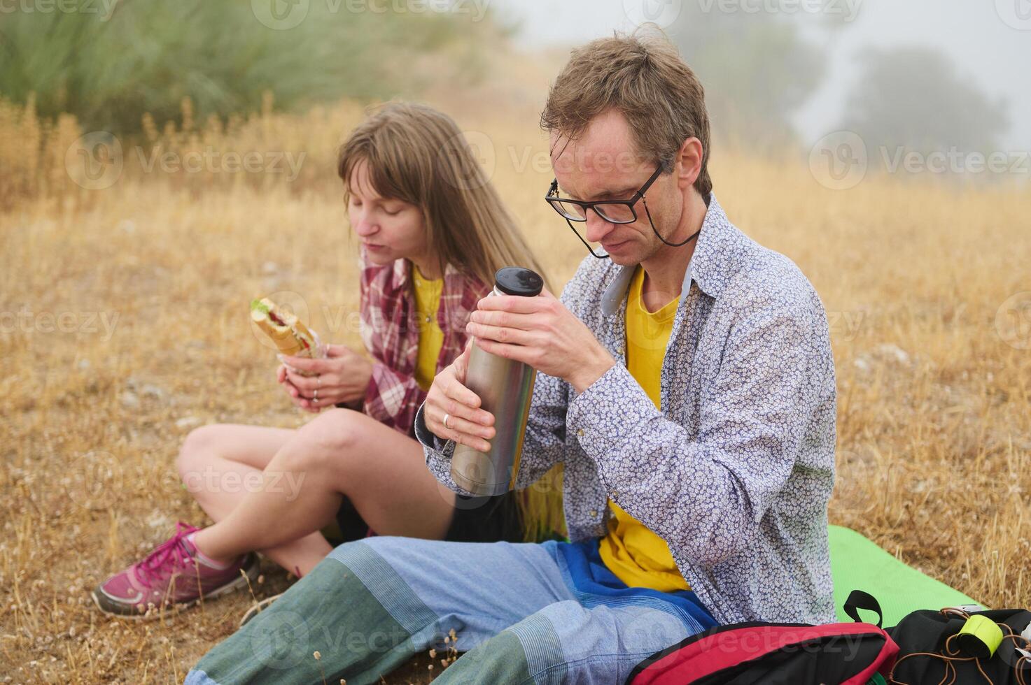 Couple Enjoying A Picnic Break in Nature While Hiking Through a Grassland Area photo