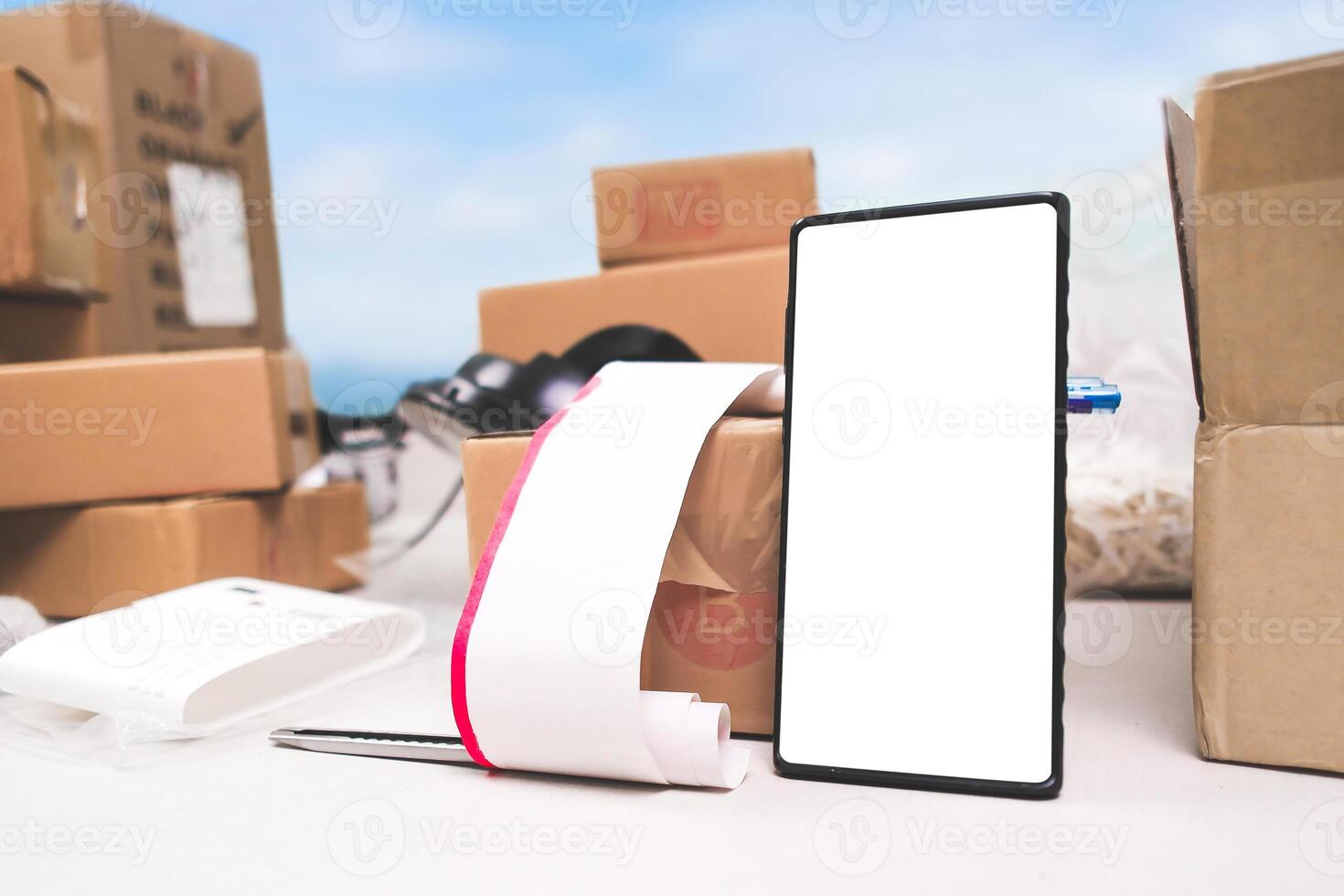 Smartphone with blank screen and receipt on table surrounded by cardboard boxes for online delivery. photo