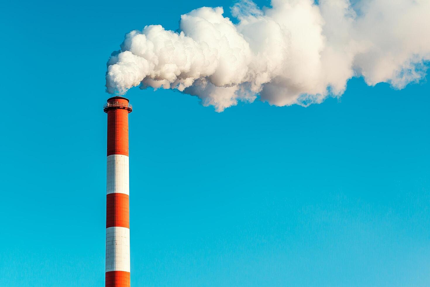 Industrial smokestack releasing thick white smoke against a clear blue sky. Environmental impact and pollution policy concept. photo