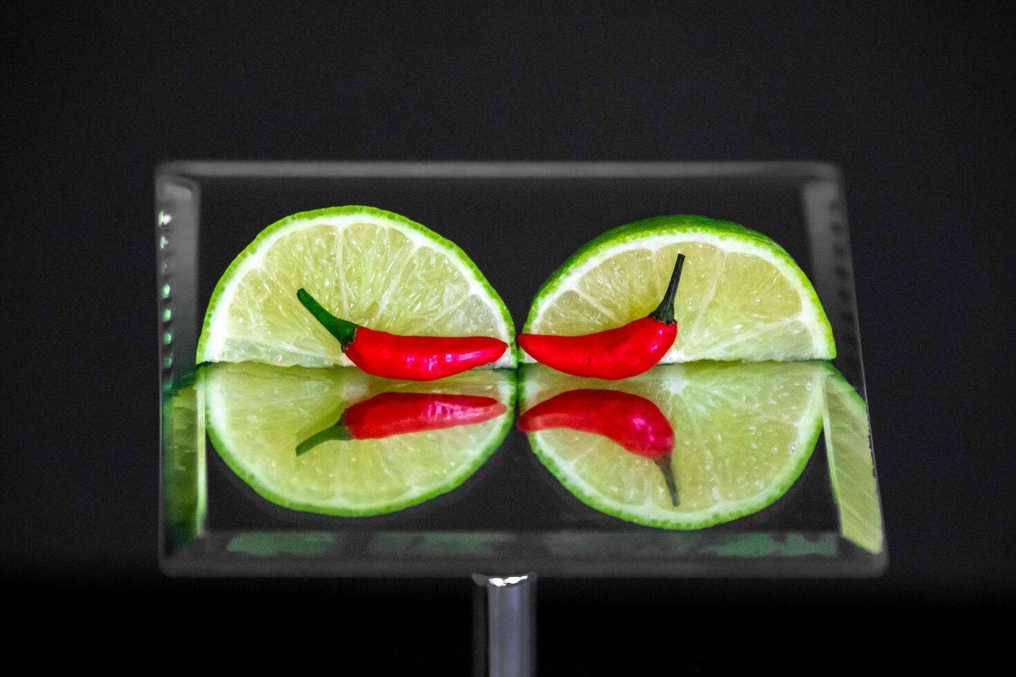 Tahiti lime cut with chili pepper on mirror with reflection closeup photo