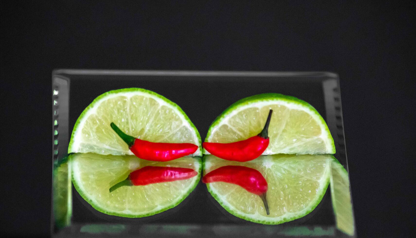 Tahiti lime cut with chili pepper on mirror with reflection photo