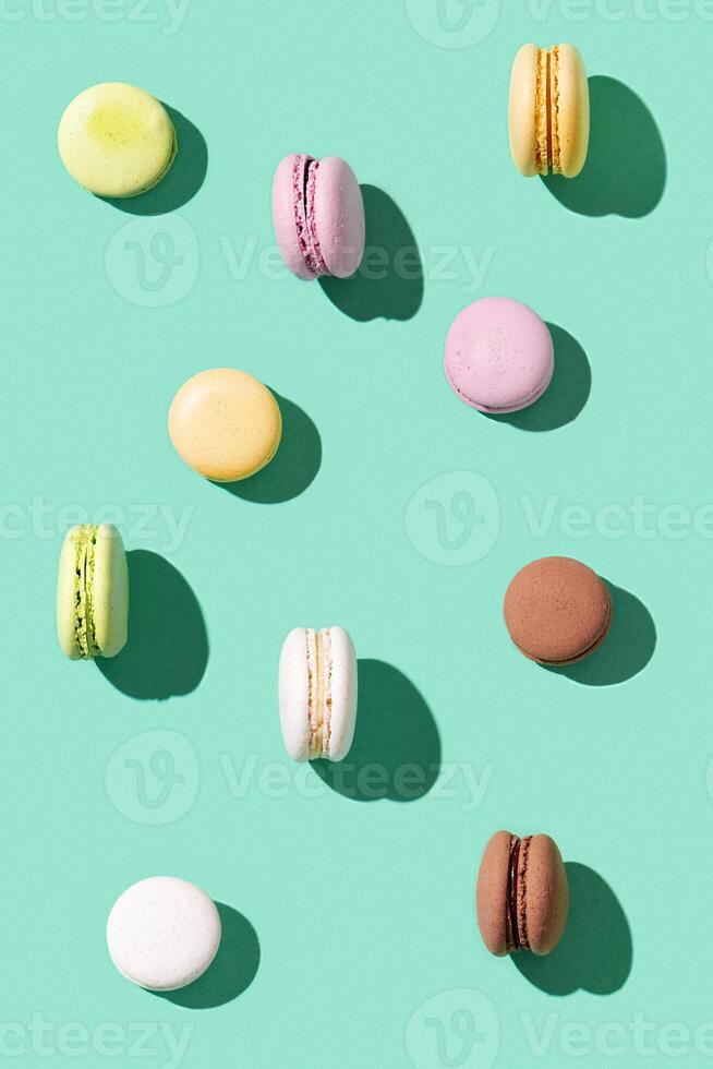 Pattern from different cake macaroons on bright blue green color background, multi colored french biscuit macarons. photo