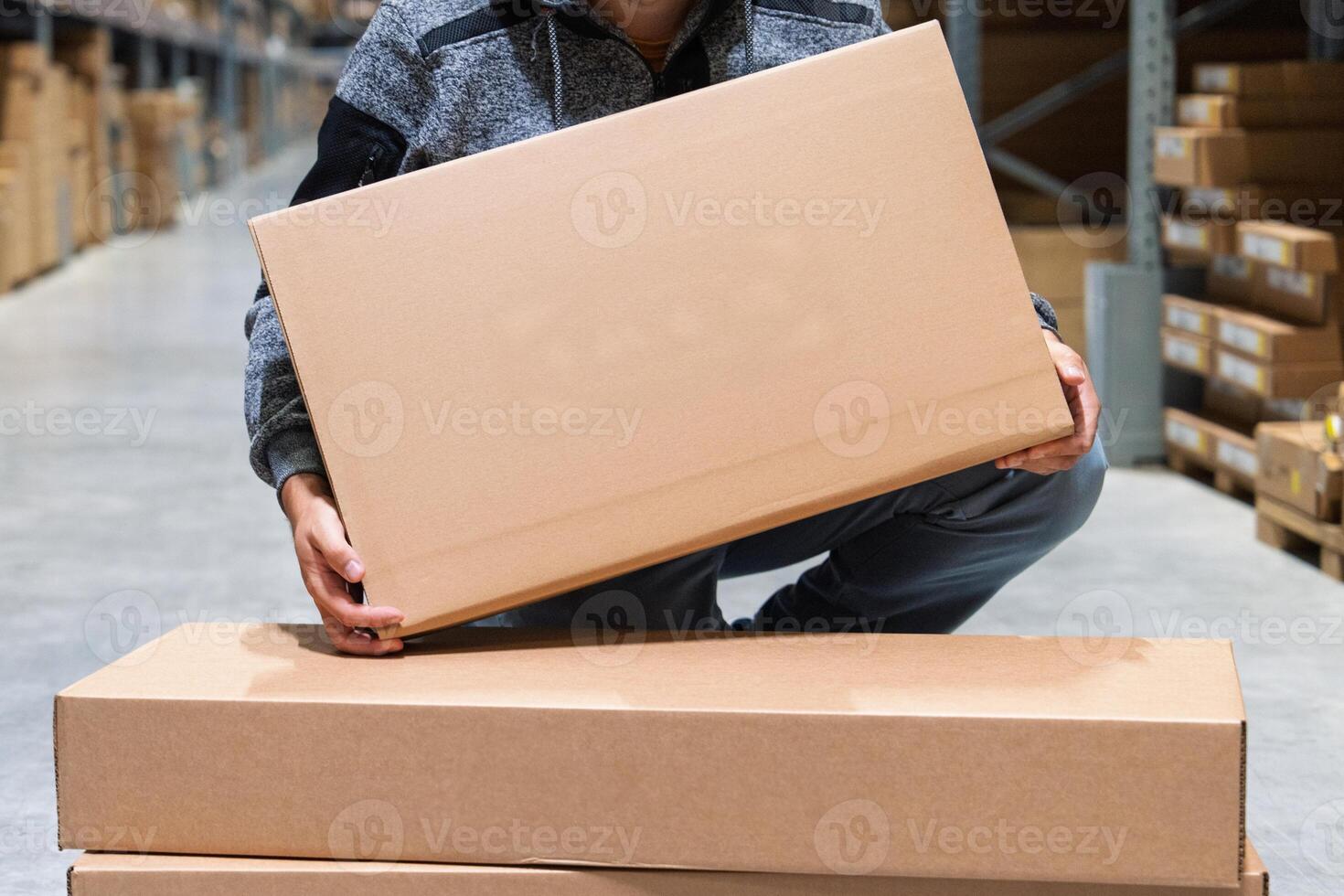 A warehouse employee lifts a large cardboard box in a busy logistics facility. The worker is focused on organizing inventory and preparing items for shipping, ensuring efficiency in the depot. photo