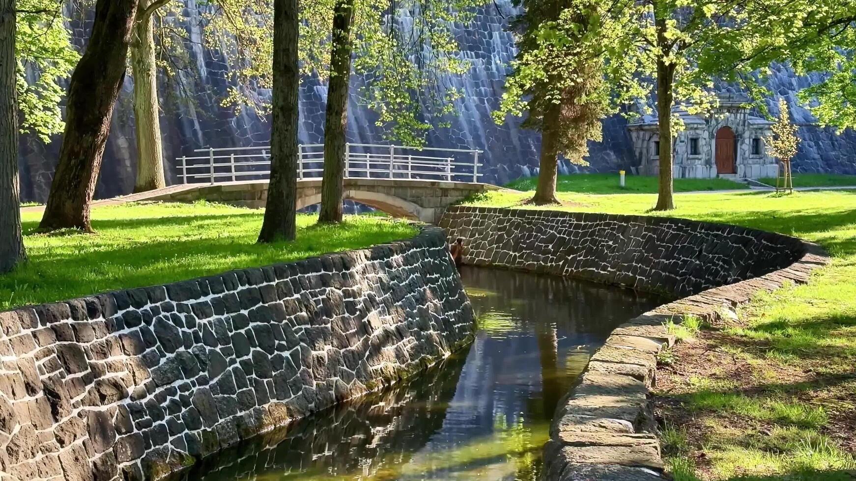 Discover a serene park with a stone wall, river, and bridge photo