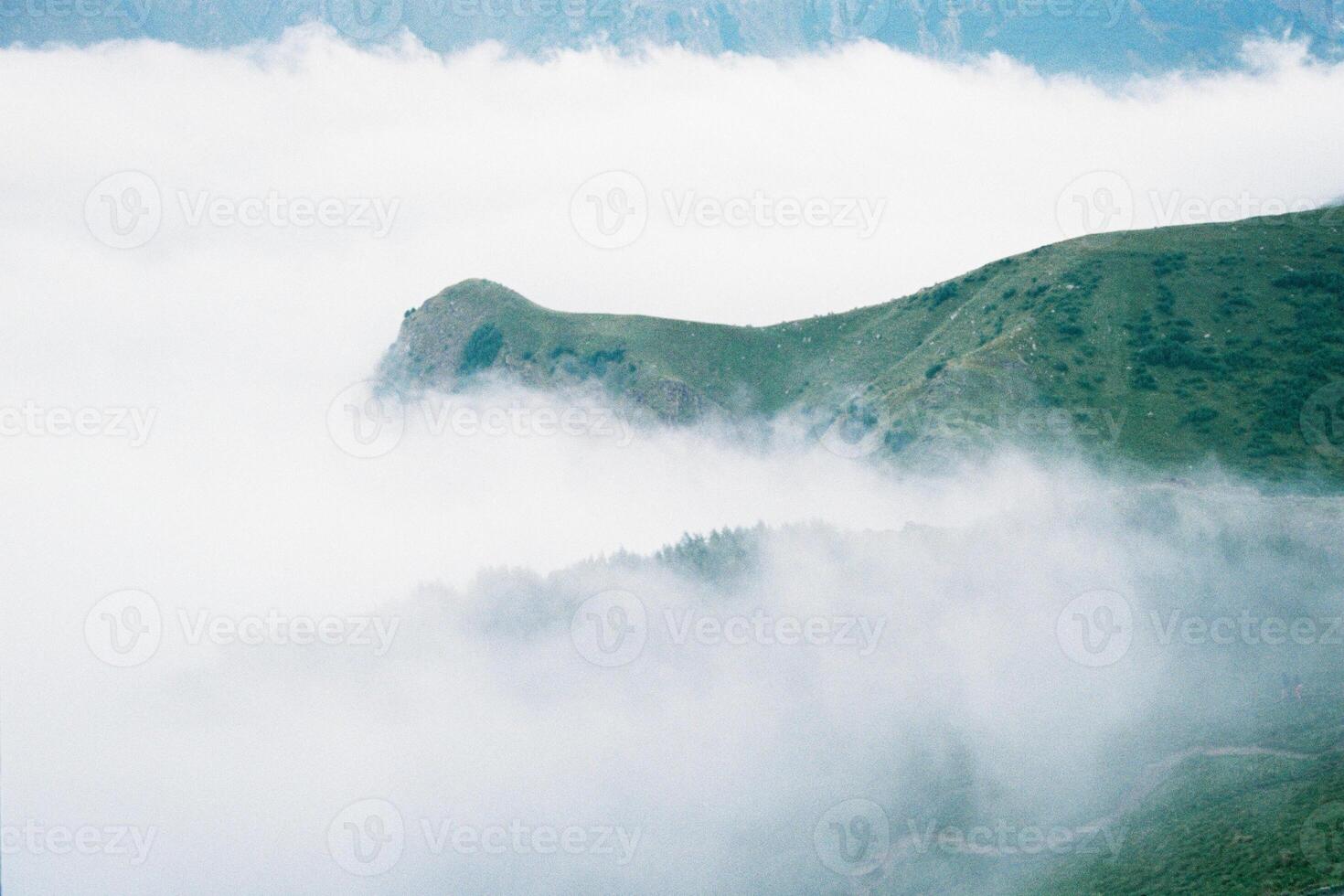 Mist of white clouds on beautiful green mountain peaks, Georgia. Grainy film in the style of old photos