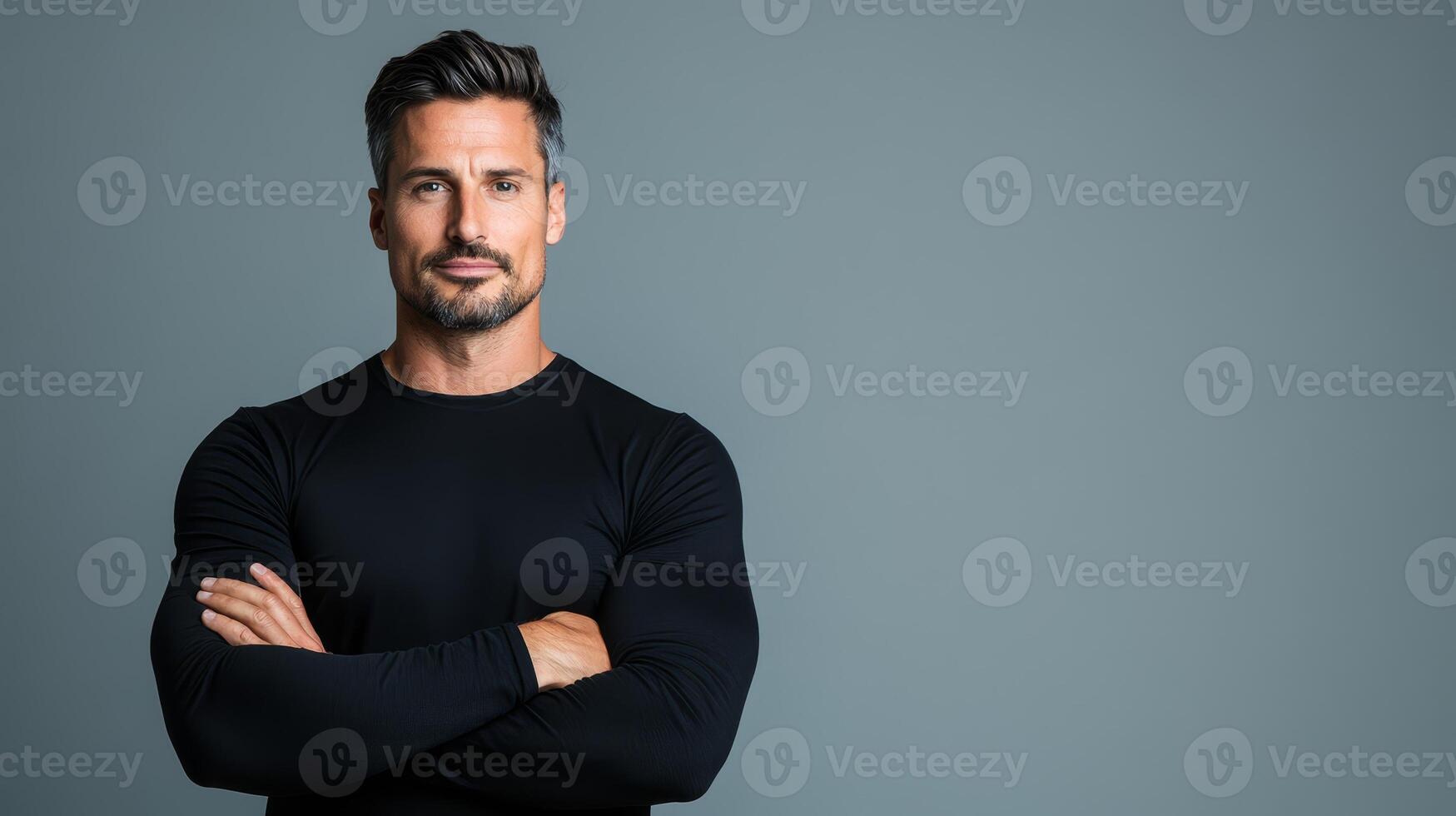 A muscular man stands confidently with crossed arms in a studio setting, showcasing strength and charm in a neutral environment photo