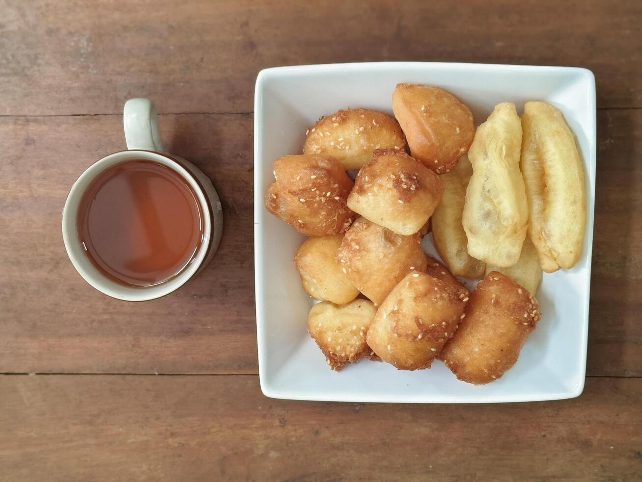 Bolang baling, Odading, fried bread in cubes or blocks, with a light brown crunchy outer skin and sprinkled with sesame seeds with cup of tea on brown wooden table photo