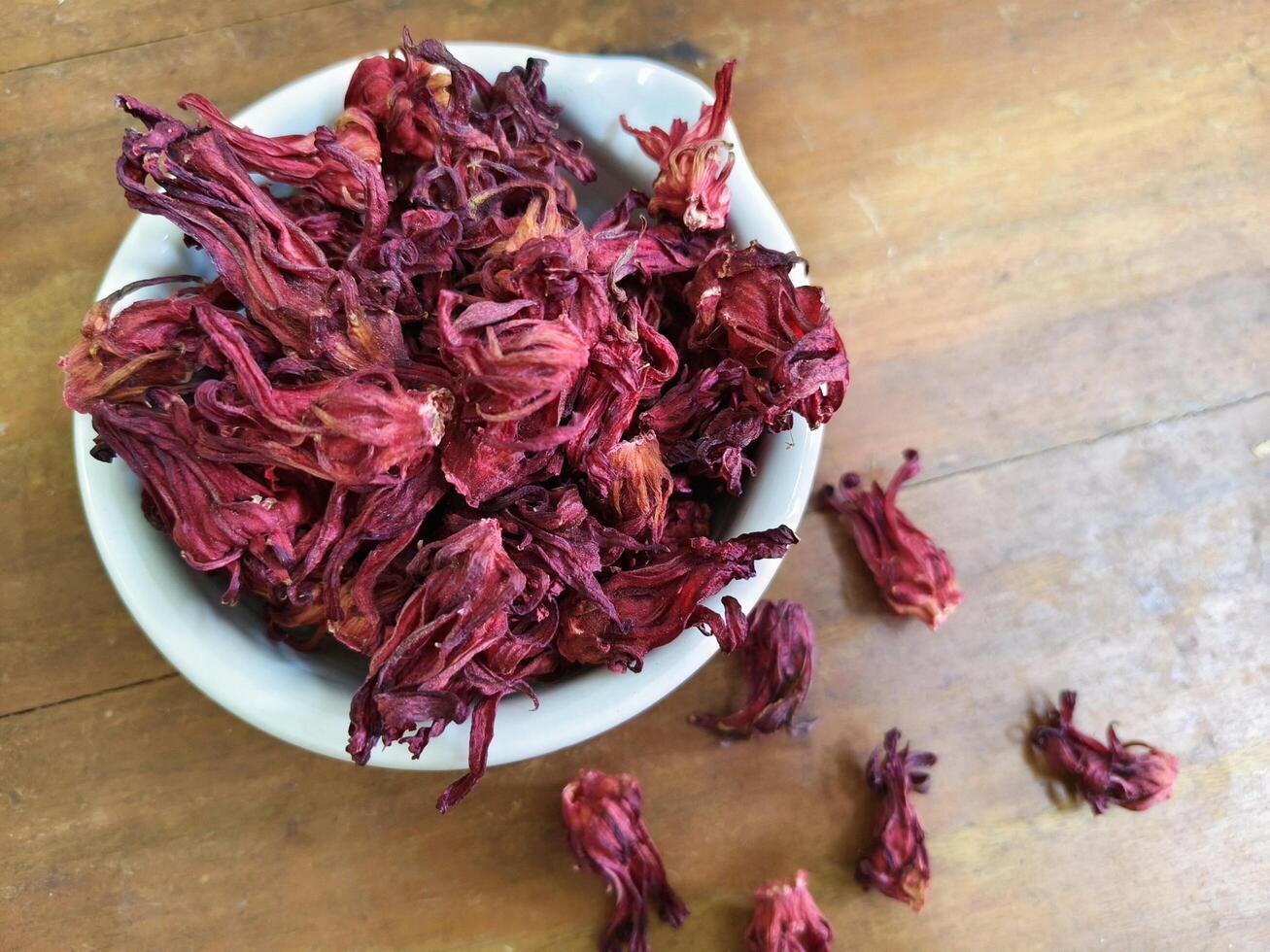 Close up of dry Roselle flower, Jamaica sorrel or hibiscus sabdariffa, in white bowl with old brown wood as background. photo