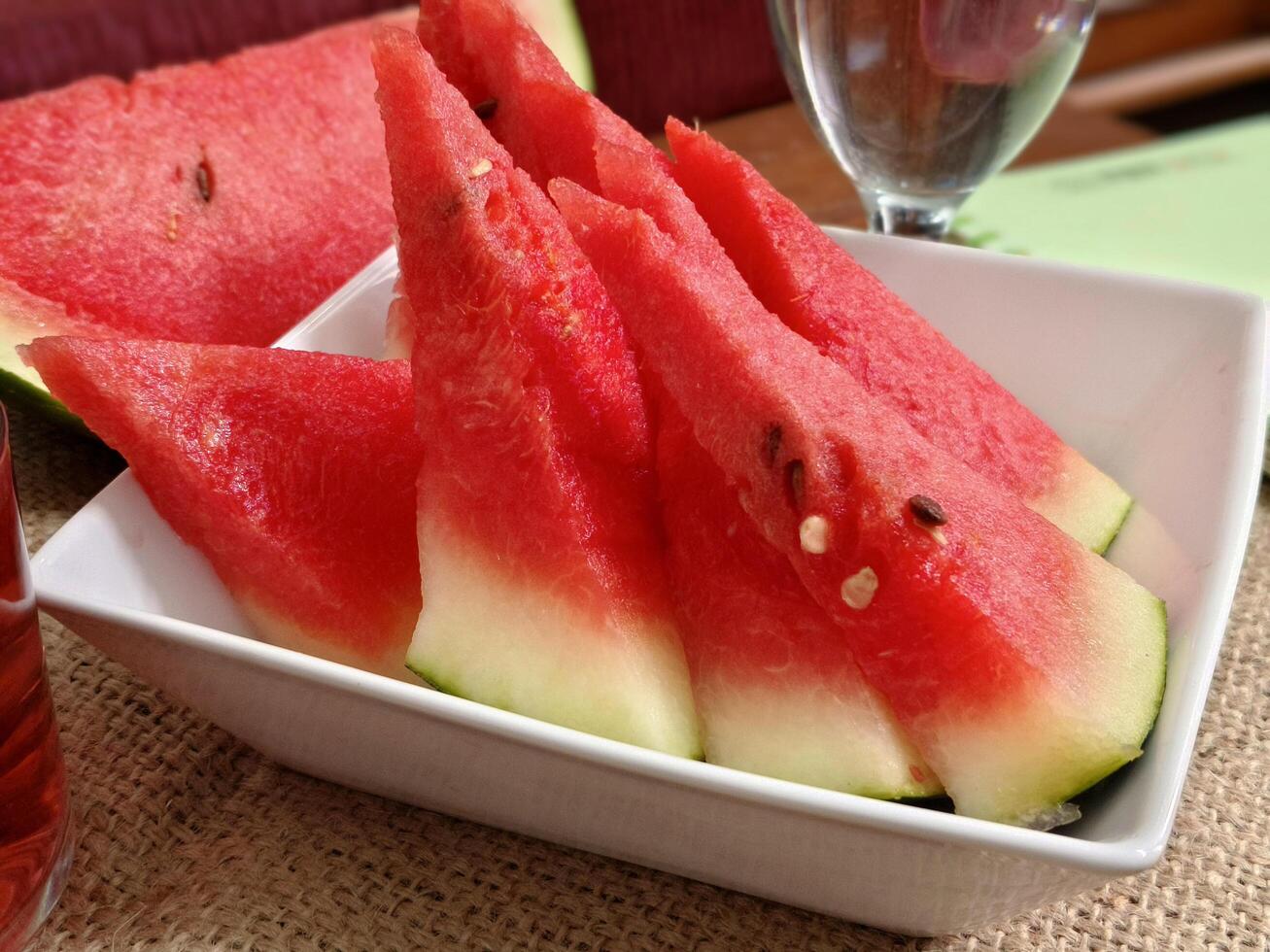 close up watermelon slices on a white porcelain serving plate and a glass of water photo