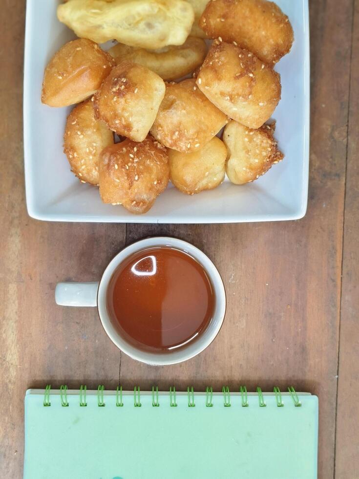 Bolang baling, Odading, fried bread in cubes or blocks, with a light brown crunchy outer skin and sprinkled with sesame seeds with cup of tea on old wooden table photo