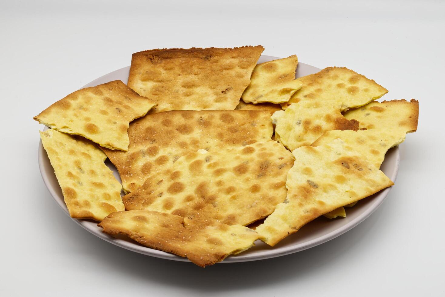 Crispy golden yellow flatbread crackers on a light plate against a white background. photo