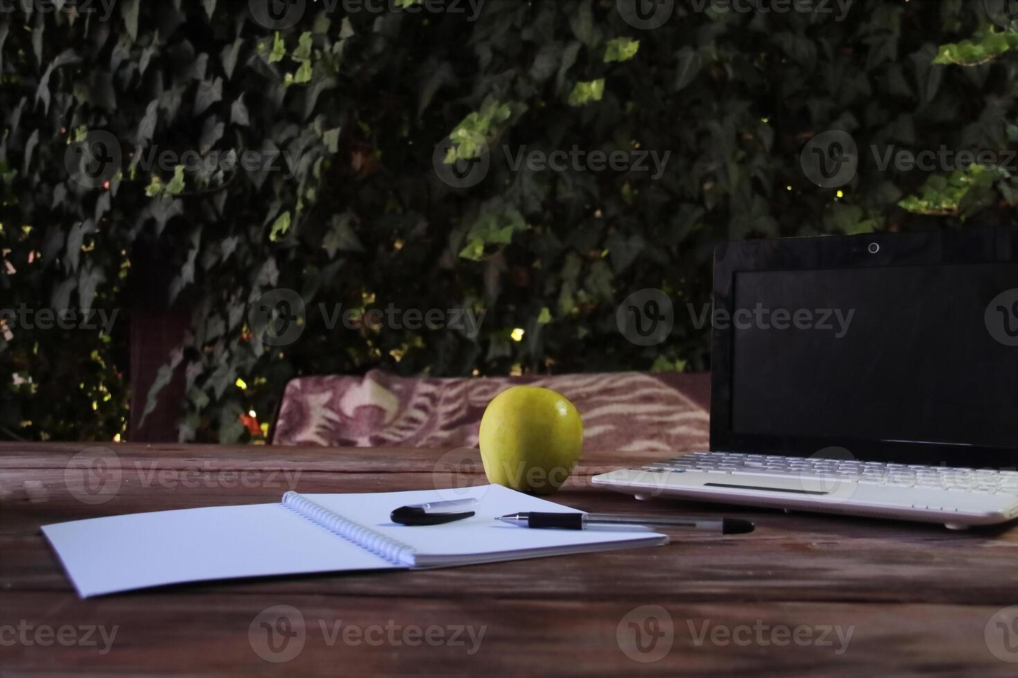 There is a laptop on the street table, and a notepad is open next to it. photo