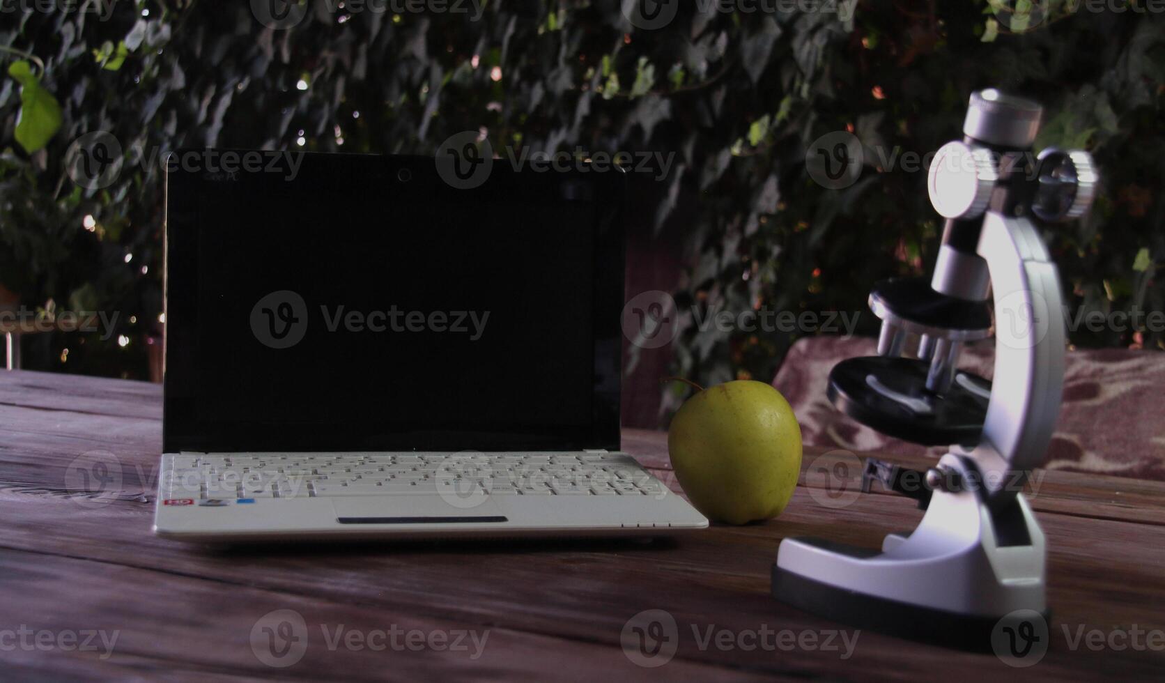 There is a microscope, a laptop, and a green apple on a wooden table. Concept of learning and research photo