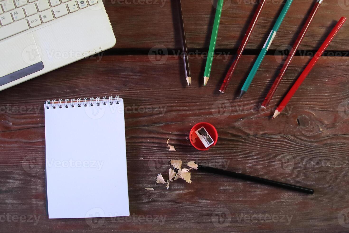 On the wooden table there is a red sharpener and pencil shavings. On the left is a notepad and a laptop. The concept of learning photo
