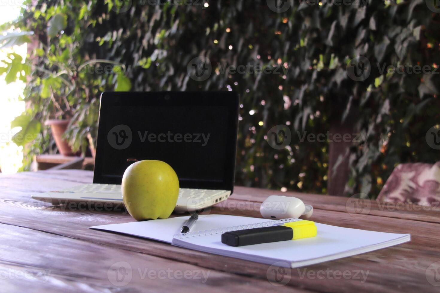 The laptop sits on a wooden table, with a notepad and a pen and bright green marker in the foreground. photo