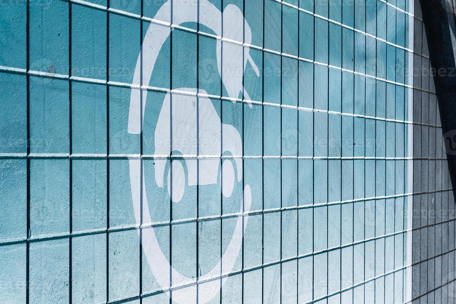 A white electric vehicle charging icon is painted on a blue tiled wall. The image represents electric mobility and sustainable transportation concepts. photo