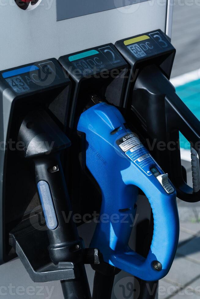 Close up of an electric vehicle charging station with multiple connectors for different charging standards. Image shows blue charging handle inserted, highlighting modern EV infrastructure and technology. photo