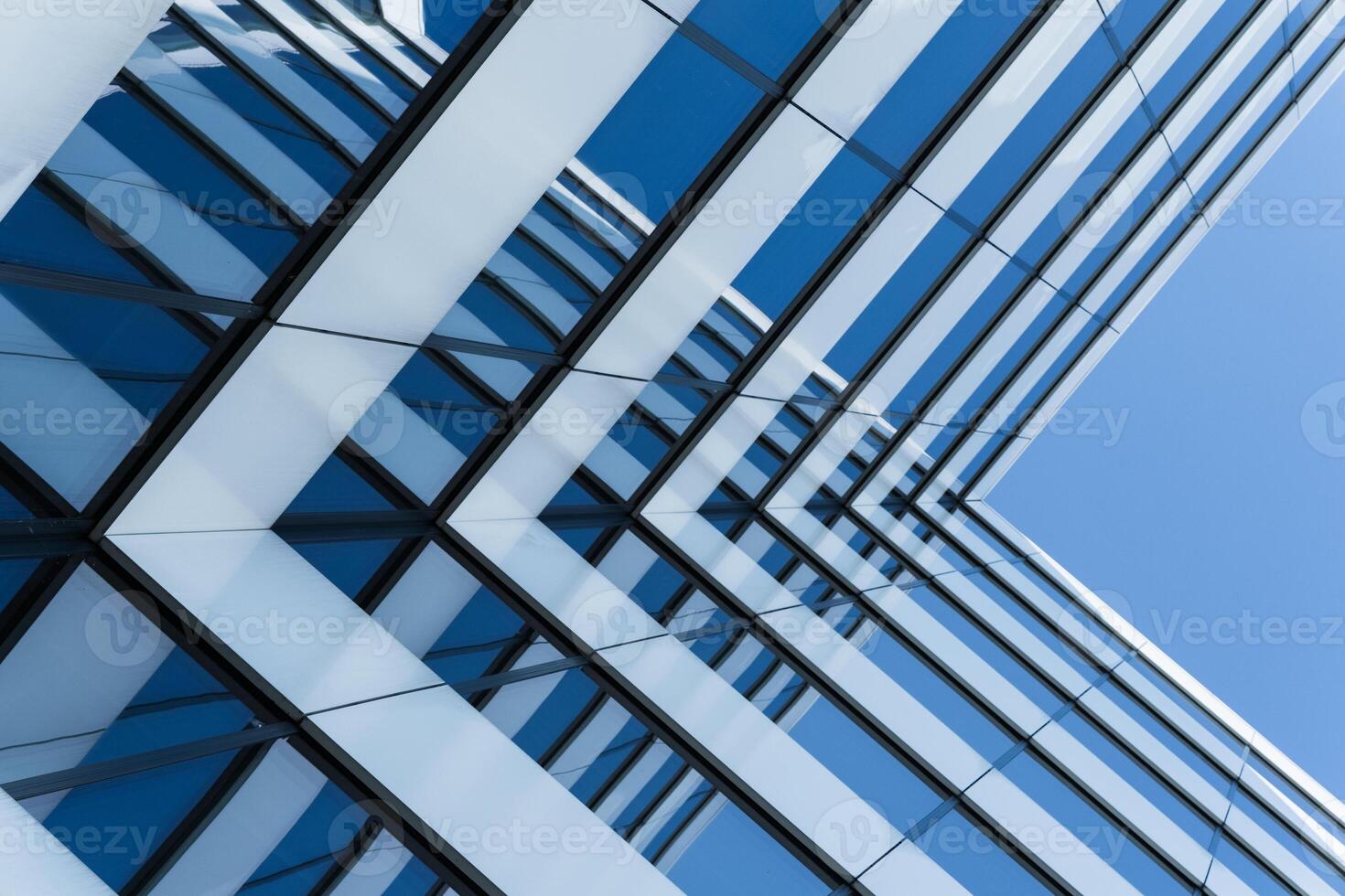 Close-up view of a contemporary glass office building with geometric lines reflecting a clear blue sky. The image emphasizes modern architecture and urban design for business or construction concepts. photo