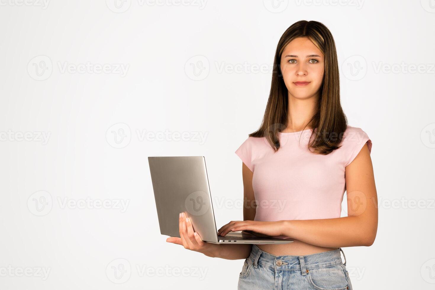 Teenage girl with straight brown hair wearing a pink t-shirt and denim shorts holds a laptop, isolated on white background. Suitable for technology, education, online learning, remote work, and youth lifestyle concepts. photo