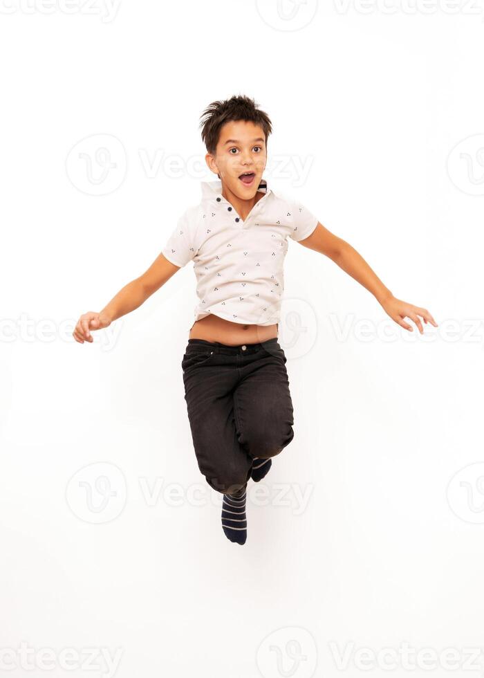 Young boy with dark hair and casual clothes is jumping with an excited expression, isolated on a white background. Suitable for concepts related to childhood, energy, happiness, and playful activities. photo