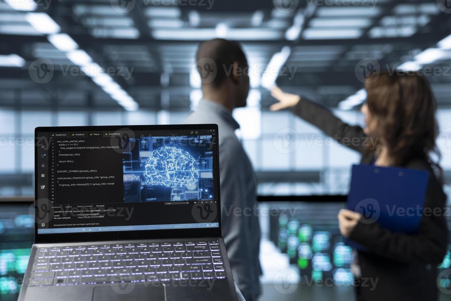 Laptop in front of data center technicians in blurry background deploying AI driven management tools, inspecting server clusters, updating network topologies, validating storage integrity photo