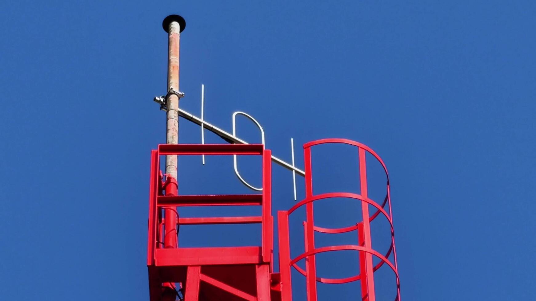A striking red communication tower stands tall against the brilliant, clear blue sky above photo