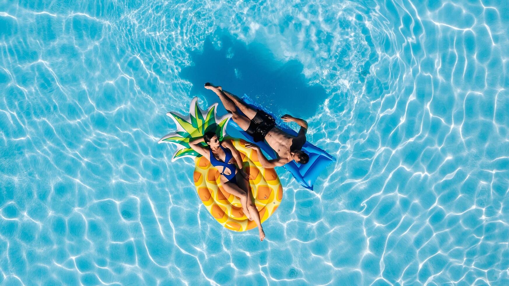 Joyful young couple relaxing on inflatable floats in an outdoor pool, drone perspective. Concept love, summer fun, freedom and tropical vibes photo