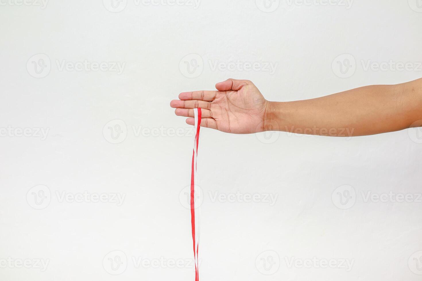 Hand holding a red and white striped ribbon against a plain white background in studio photo