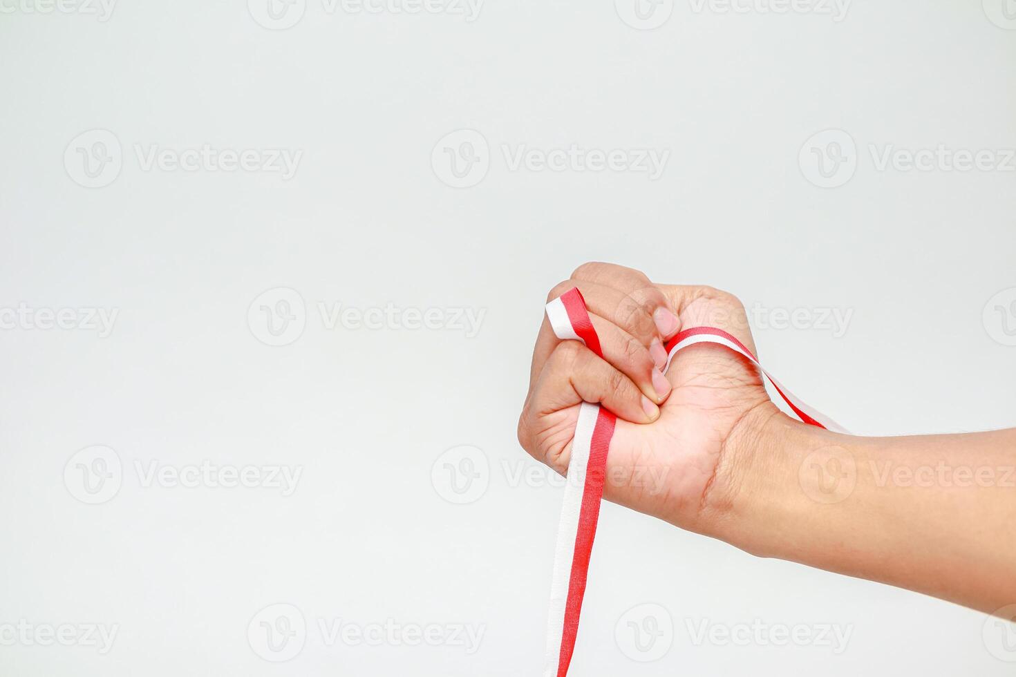 A hand clenched around a red and white ribbon on a plain background creating a sense of solidarity photo