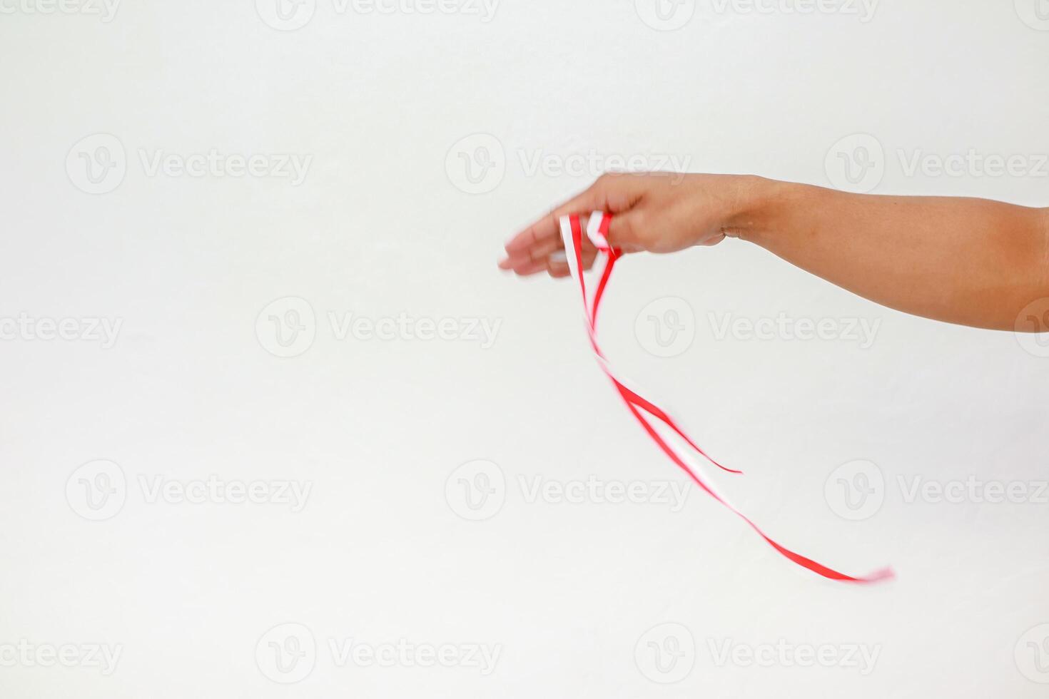 Hand holding a red and white ribbon against a plain white background in studio photo