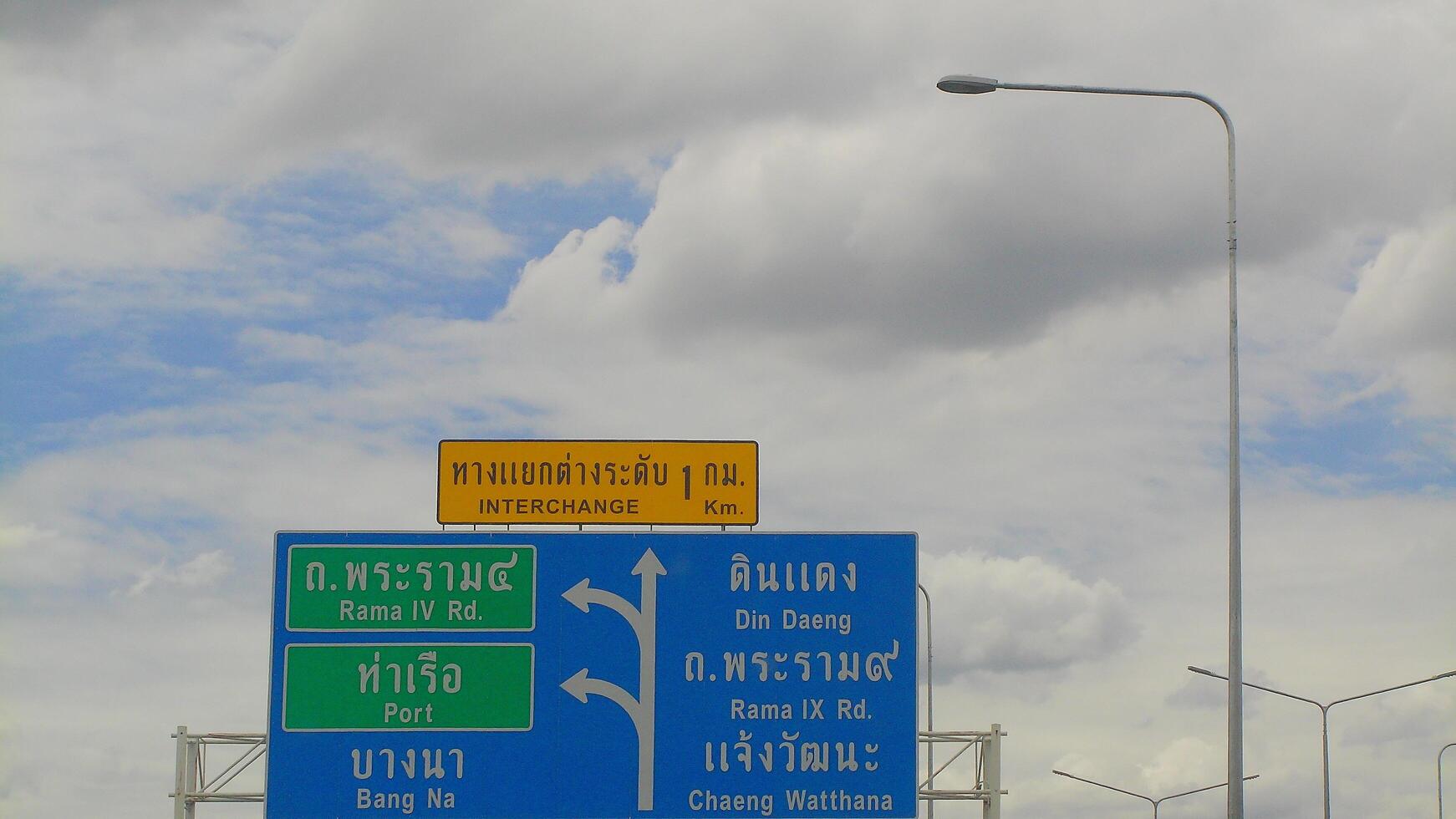 Close-up view of bright Thai expressway signs with bilingual directions under a partly cloudy sky, illustrating highway navigation in Bangkok. photo