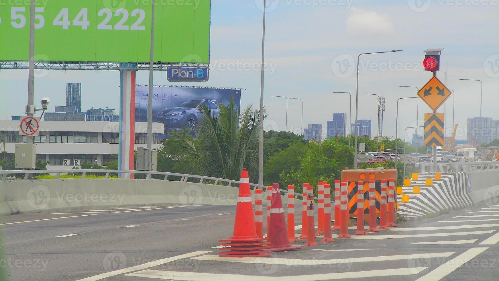 A view of an expressway under construction in Bangkok, marked by cones, directional signage, and billboard advertisements in the background. photo