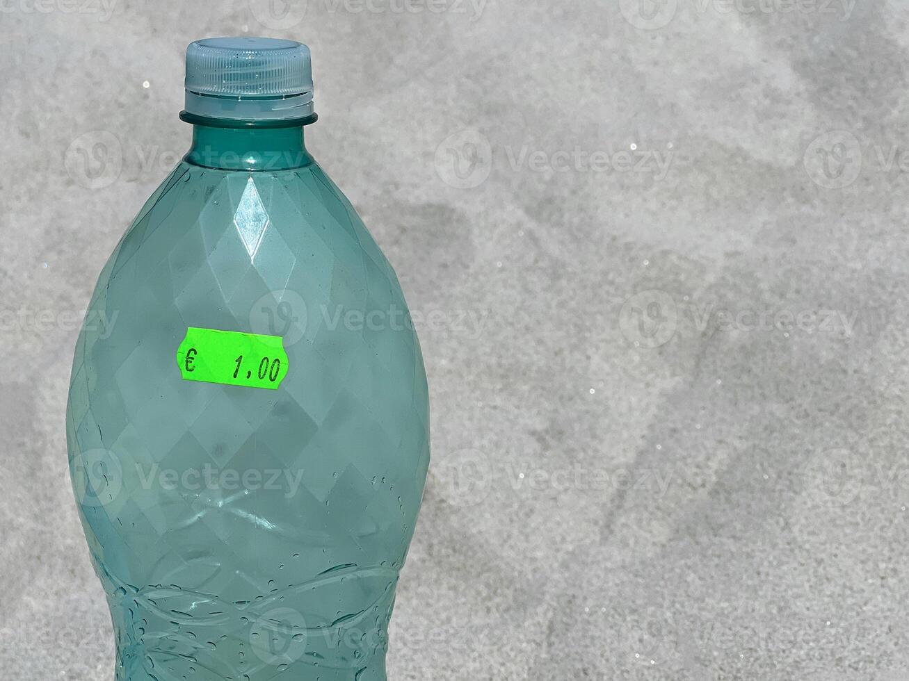 A plastic water bottle with 1 euro price sticker at the background of a beach sand on a hot summer day photo