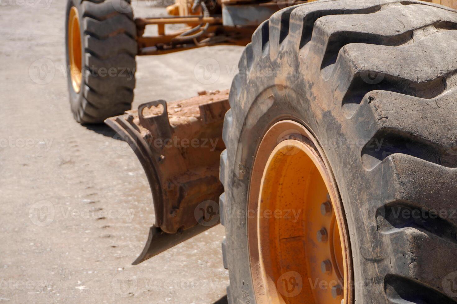 A close-up view of a large, rugged tire with deep treads, showcasing an orange rim. The background features a dusty surface, hinting at construction activity. photo