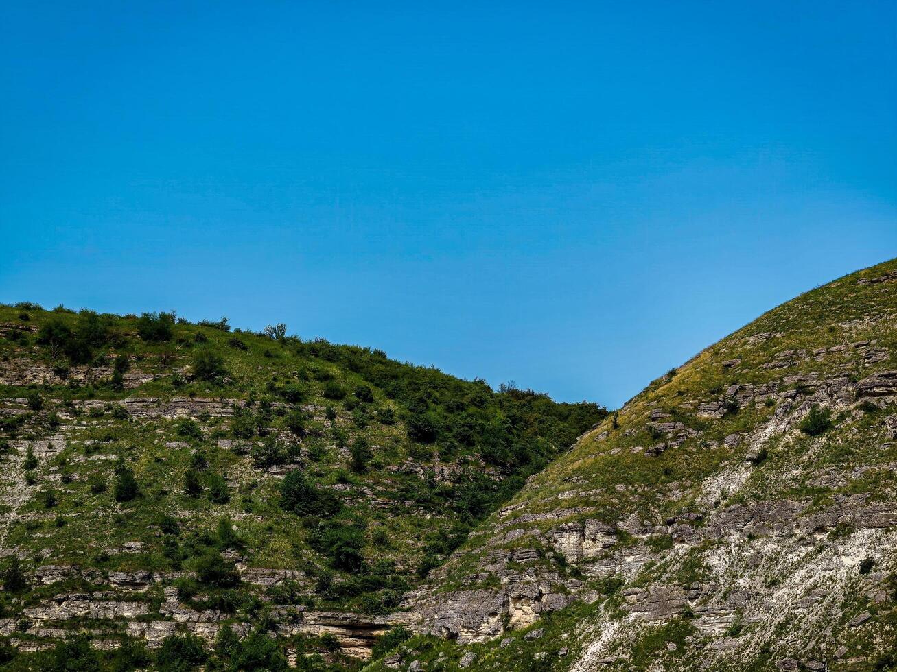 A beautiful mountain landscape with a blue sky above. The hills are covered in lush green grass and trees, creating a serene and peaceful atmosphere. The combination of the natural elements photo